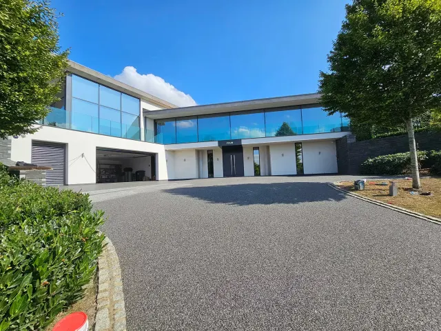 Charcoal resin bound driveway sweeping up to a modern glass-fronted house