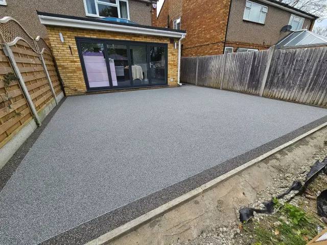 Silver-grey resin bound patio behind a brick extension with bifold doors