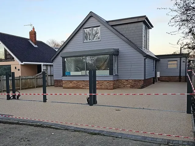 Cream resin driveway with steel bollards in front of a grey clad house