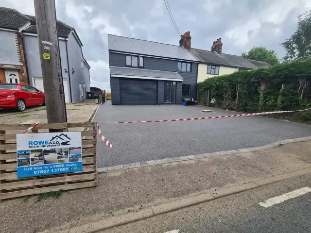 Wide charcoal resin driveway across the front of a black weatherboarded house