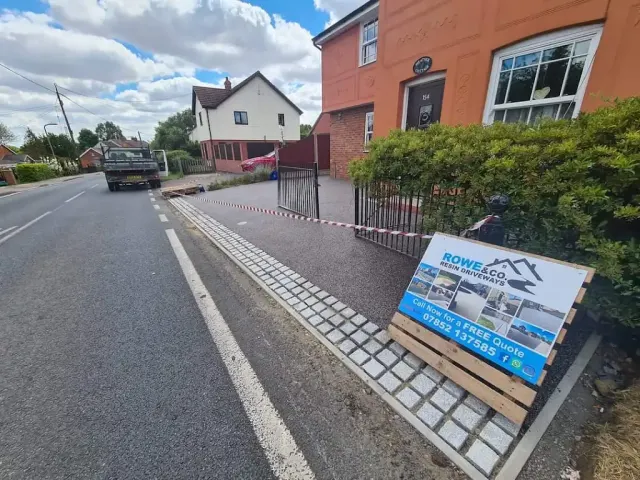 Resin driveway behind railings with a granite sett channel at the kerb