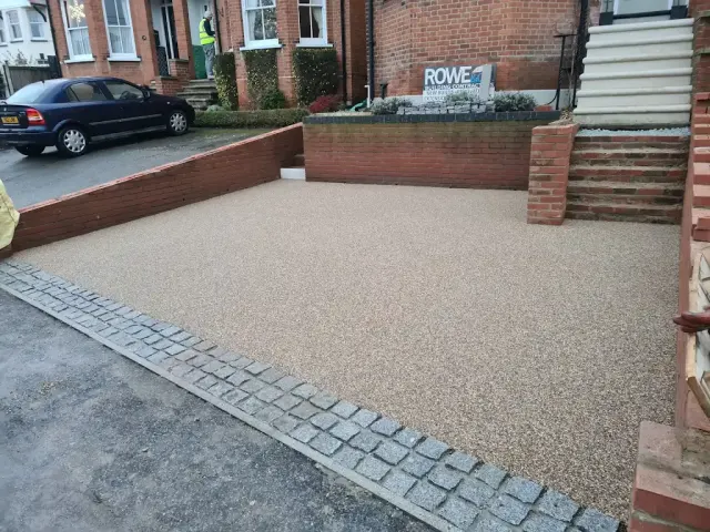 Gold resin driveway edged with granite setts between low brick walls