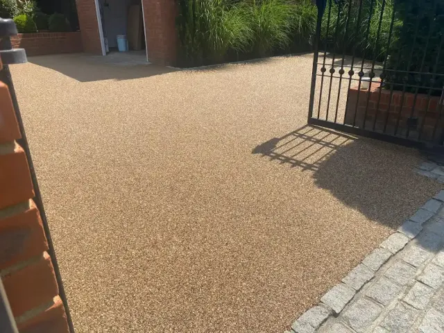 Gold resin driveway with a granite sett edge inside iron gates