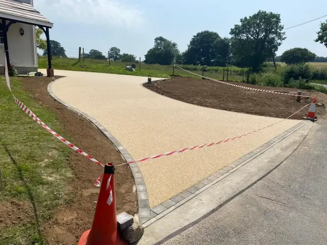 Curved cream resin drive with a granite sett edge running through open countryside