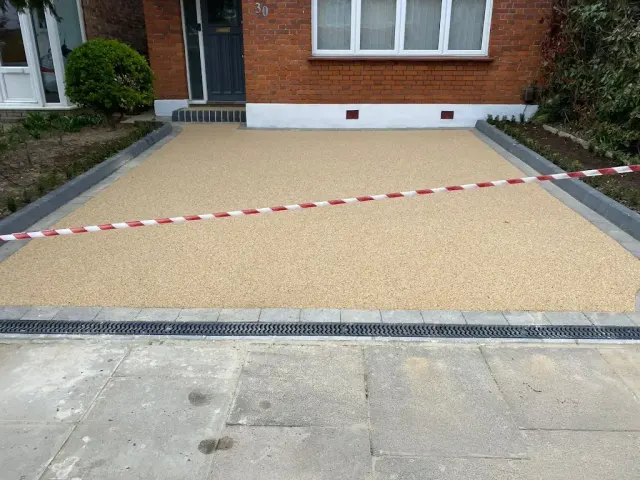 Cream resin driveway with a channel drain across the entrance