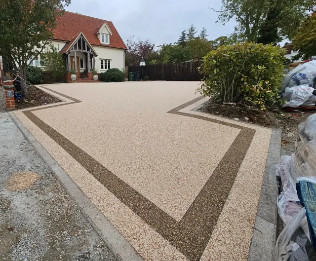 Cream resin driveway with a bronze border band in front of a tiled cottage