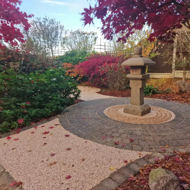 Buff resin garden path curving around a block paved circle and stone lantern