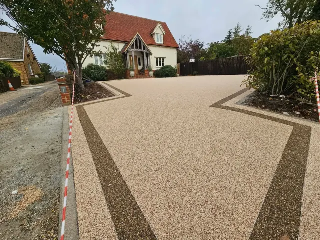 Cream resin driveway with bronze border bands sweeping up to a cottage